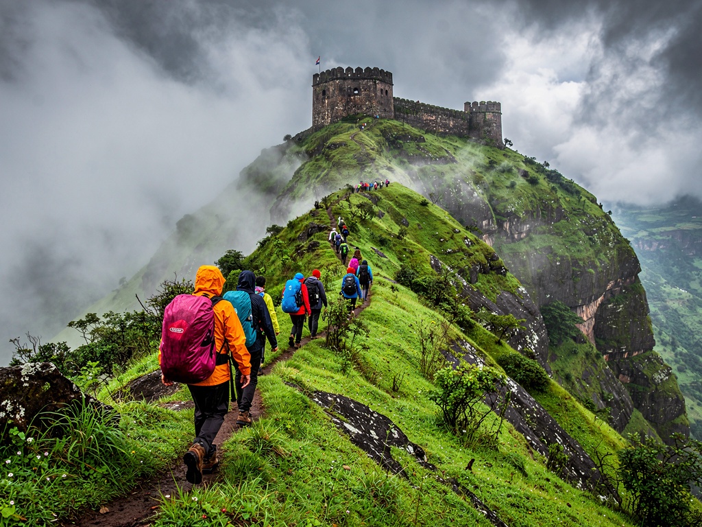 Hikers trekking up a green ridge towards a hill fort near Lonavla