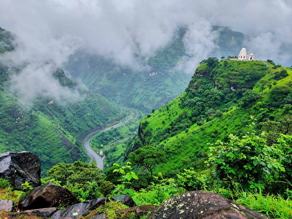 A scenic Khandala viewpoint with green hills, a winding valley road and mist